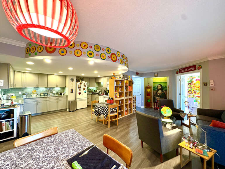 Wide-angle view of colorful open-concept kitchen and living room with red pendant lamp and yellow decorative plates.
