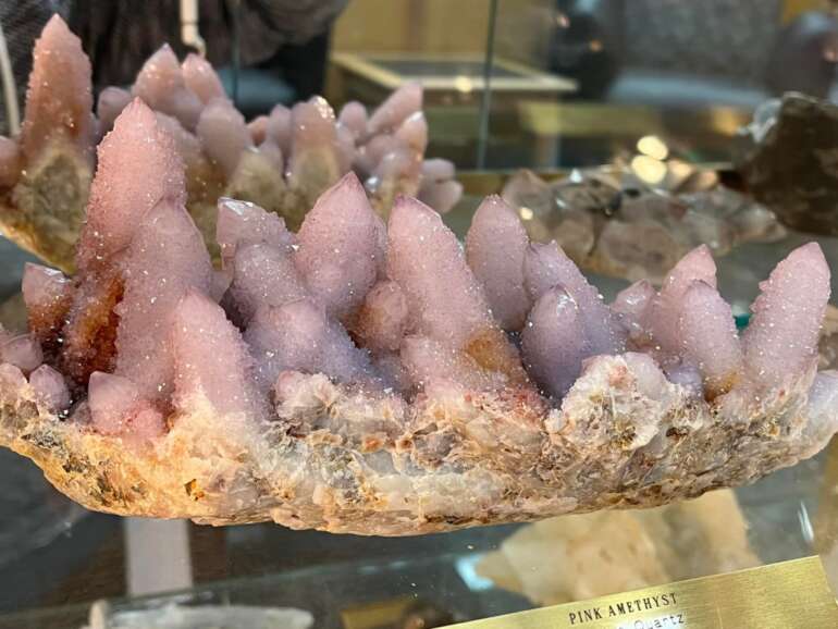 Want To See Some Of The Rarest Minerals In The World? Head To Celina, Ohio 19 Close-up of pink amethyst quartz crystals with pointed formations on tan mineral base in museum display case.