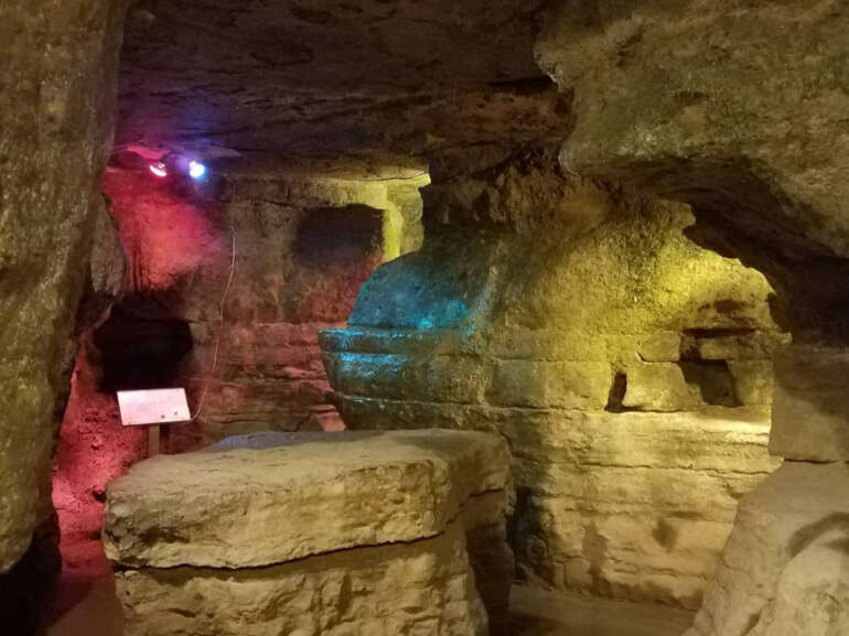 It’s 90 Degrees Outside, But Always 55 In These Caverns Near Columbus 3 Underground stone chamber with colorful LED lighting illuminating carved walls and statues.