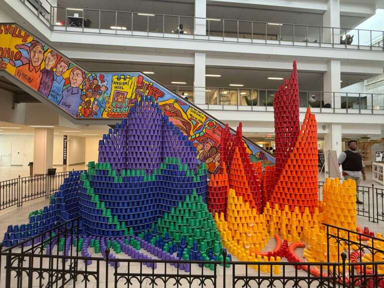 This Wild Cup Sculpture At The Columbus Library Is About To Come Crashing Down 3 Colorful stacked cups installation creating castle and tower shapes in modern indoor atrium space.