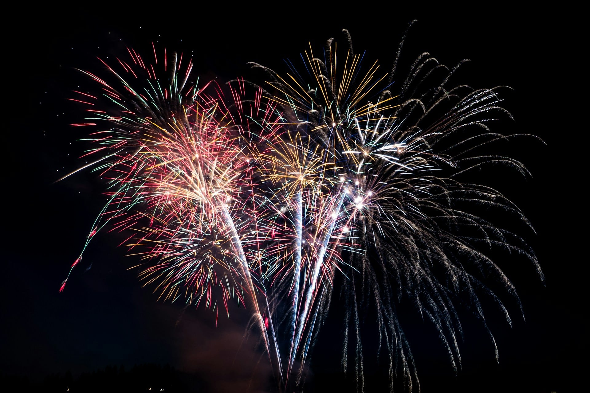 Colorful fireworks burst across a dark night sky in vibrant red, gold, and blue streaks.