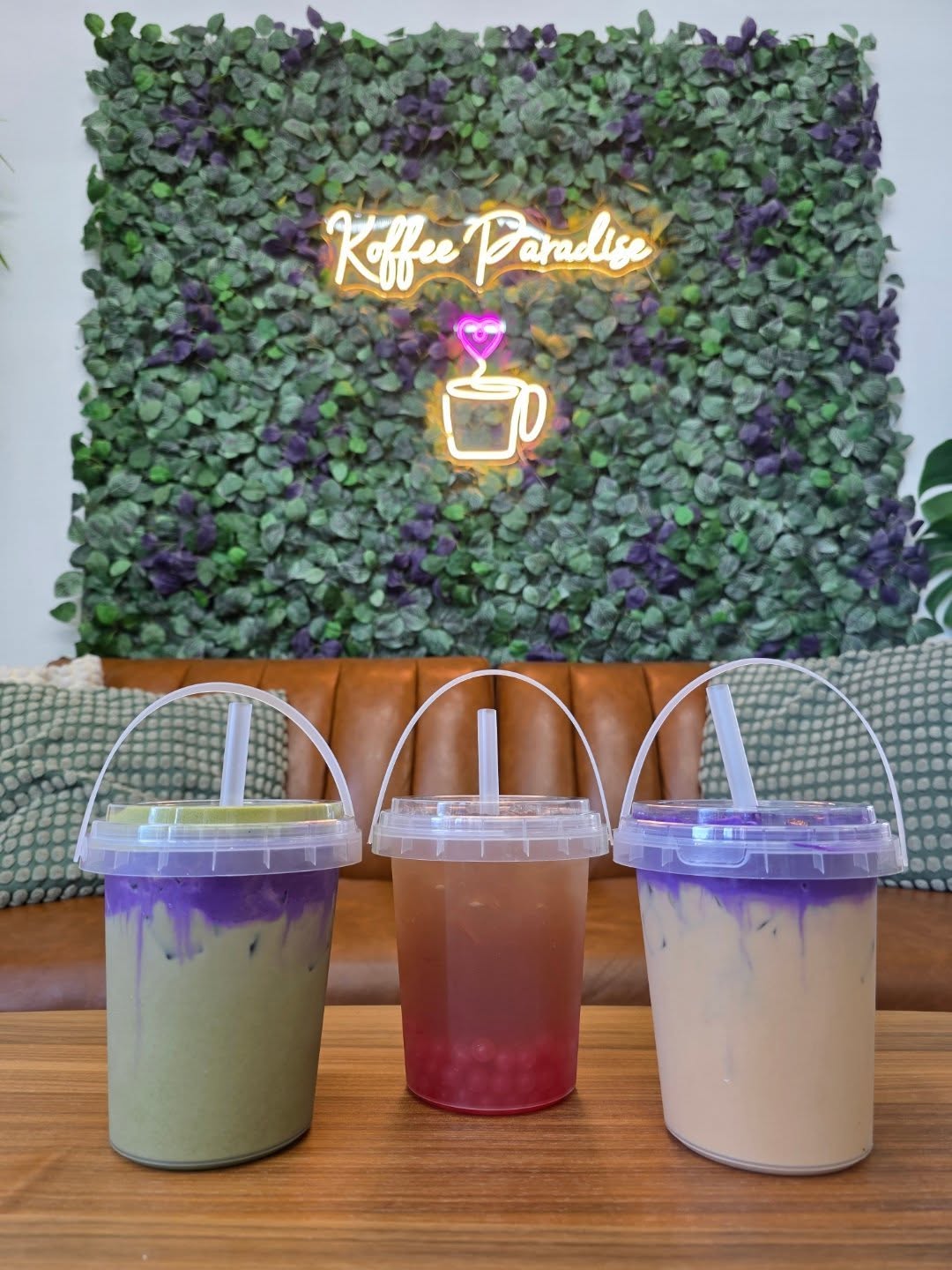 The Best New Restaurants In Columbus (August 2026) 2 large coffees in to-go containers infront of plant wall with neon sign