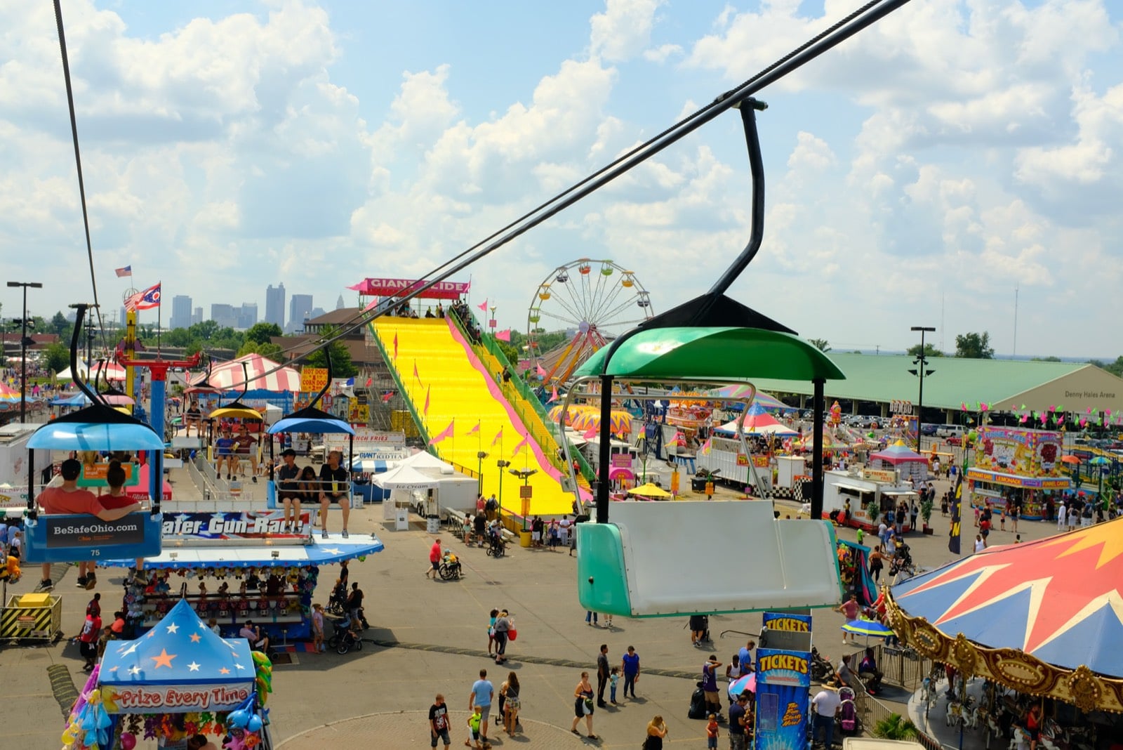 The Ohio State Fair midway, giant slide, and Ferris wheel seen from the SkyGlider, with the downtown Columbus skyline in the distance