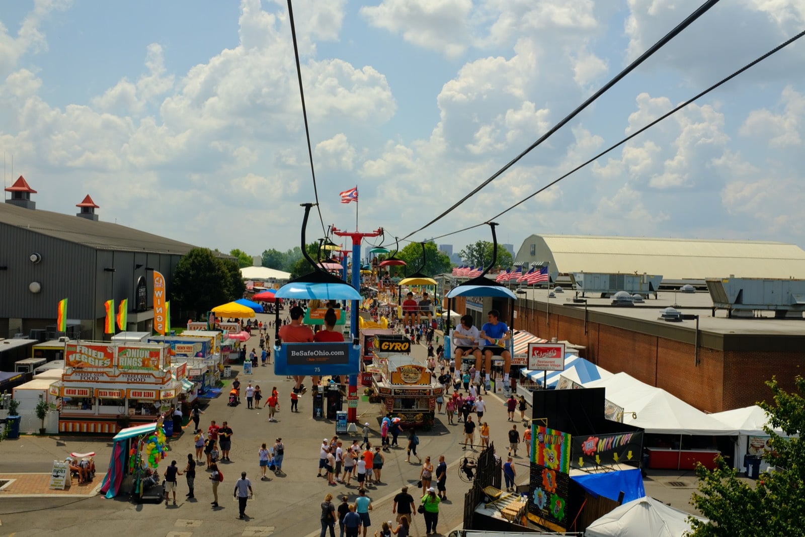 Crowds walking the Ohio State Fair midway past food stands and game booths, seen from the SkyGlider