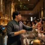 The Best Happy Hours In Columbus Bartender handing a cocktail across a crowded bar during happy hour
