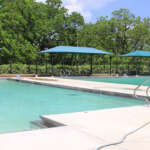 These Community Pools Around Columbus Are Open For The 2026 Season Outdoor municipal swimming pool with shade canopies on a summer day