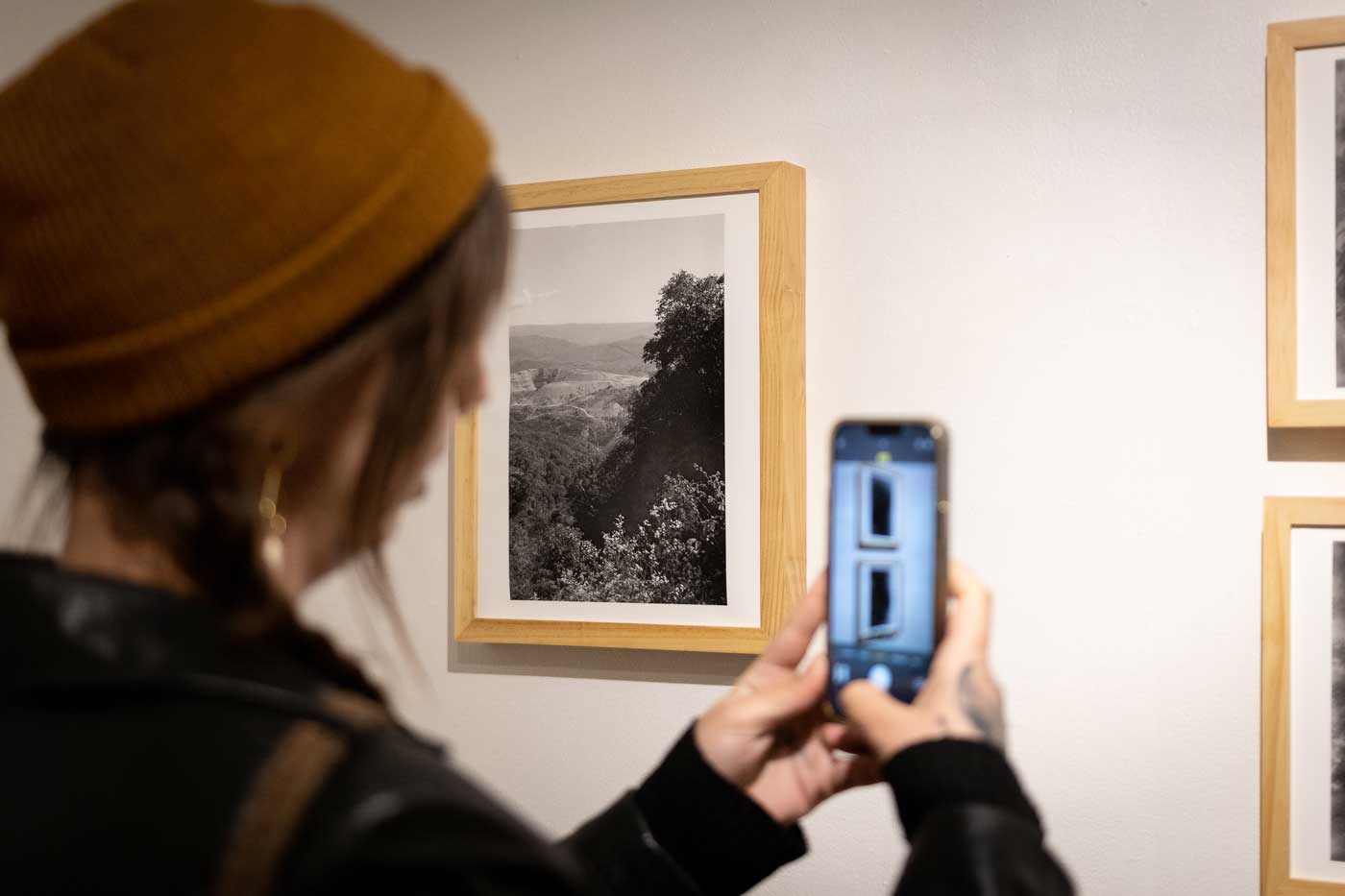 Spend Labor Day Weekend Exploring Art And More At September Gallery Hop 1 person taking photo on phone of art on gallery wall