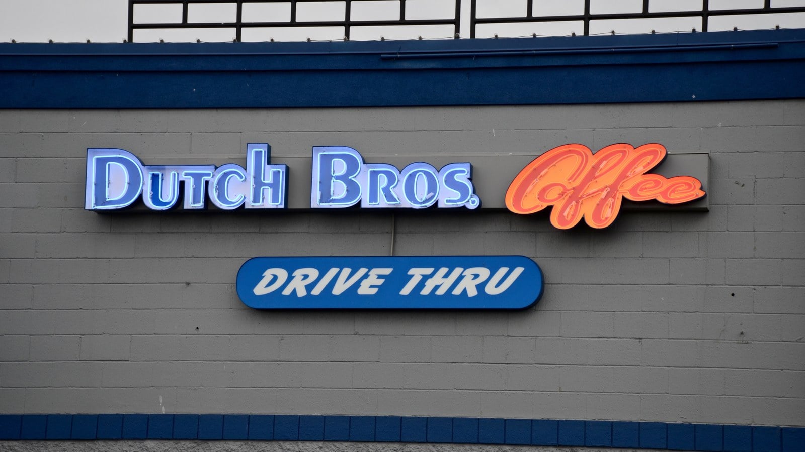 Dutch Bros Coffee neon sign and drive thru sign on a gray block wall