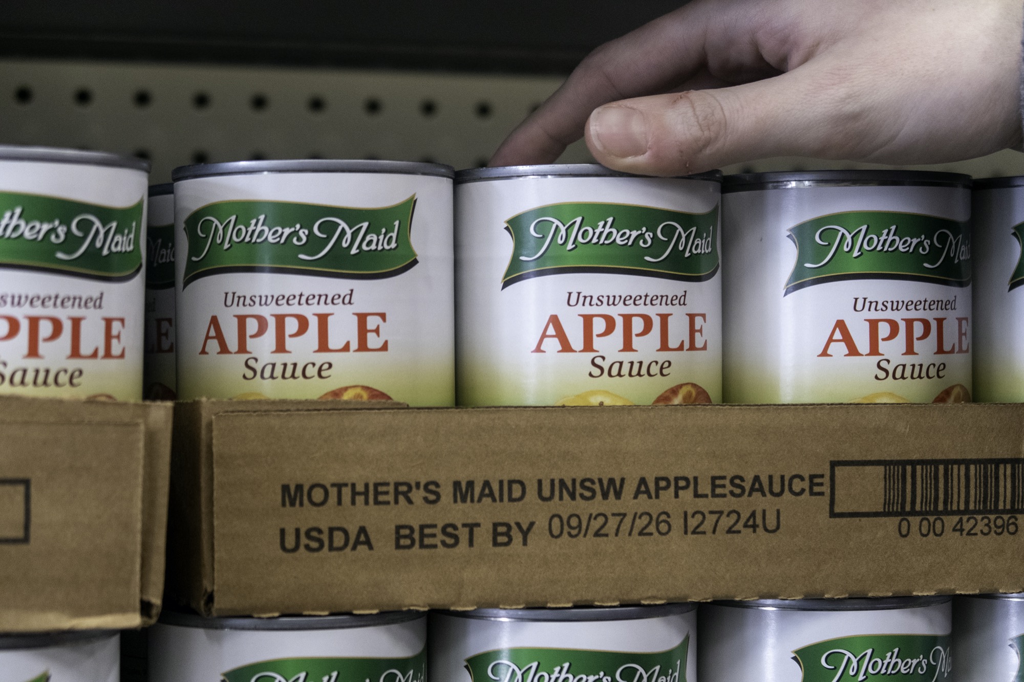 Canned applesauce lined up on a food pantry shelf