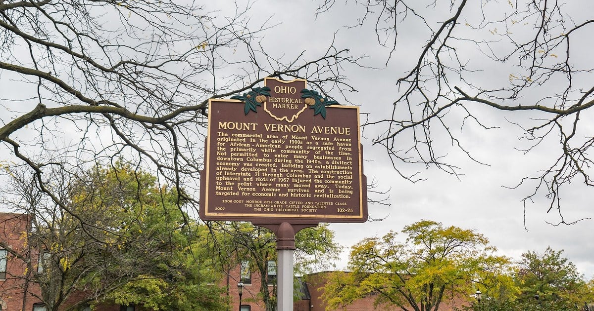 Ohio historical marker reading Mount Vernon Avenue on a pole with bare tree branches and brick buildings behind it