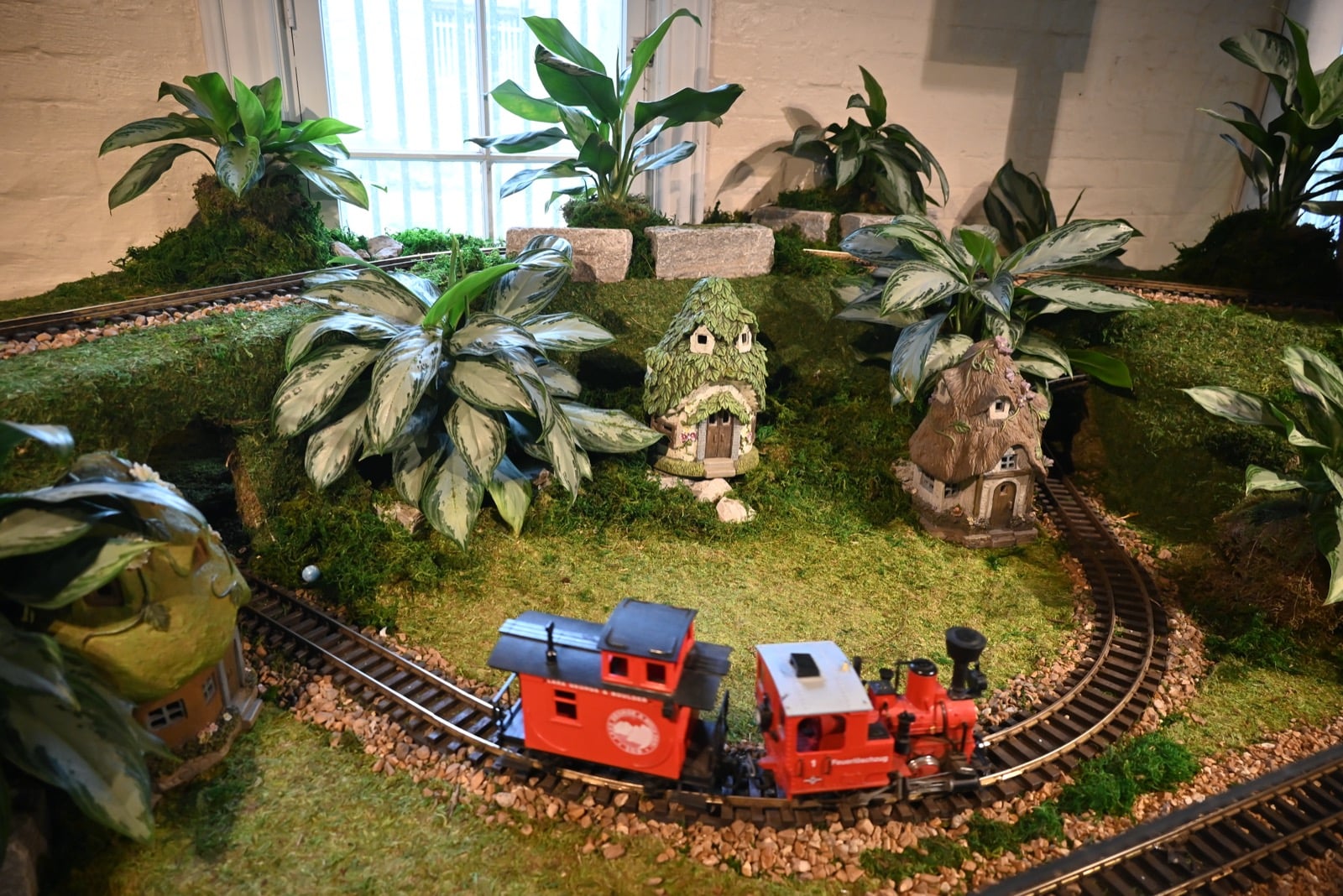 A model train rounds a curve past moss-covered miniature cottages on the Paul Busse Garden Railway at Franklin Park Conservatory