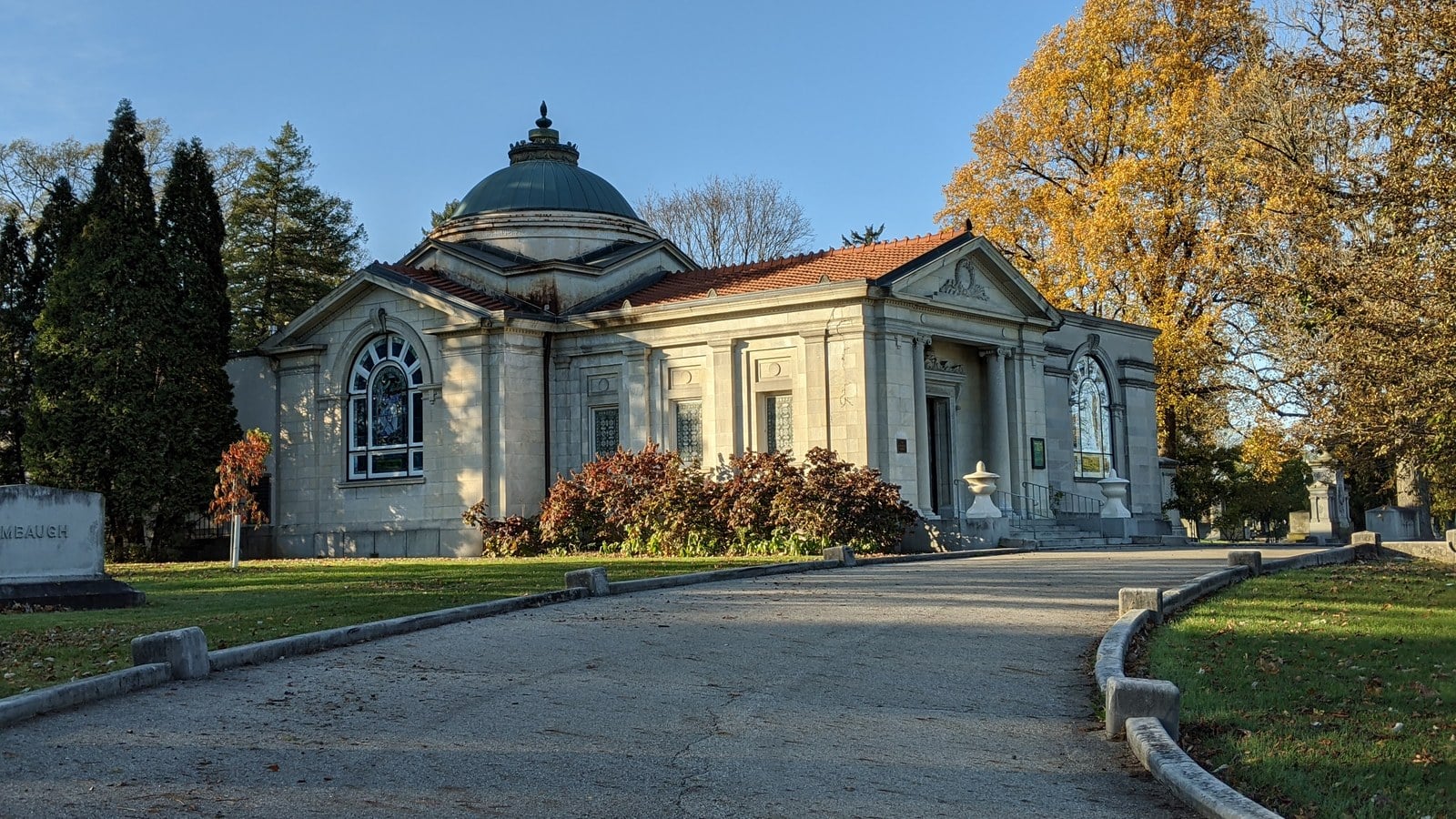 Domed limestone Huntington Chapel at Green Lawn Cemetery beside gold autumn trees, with a curving drive in front
