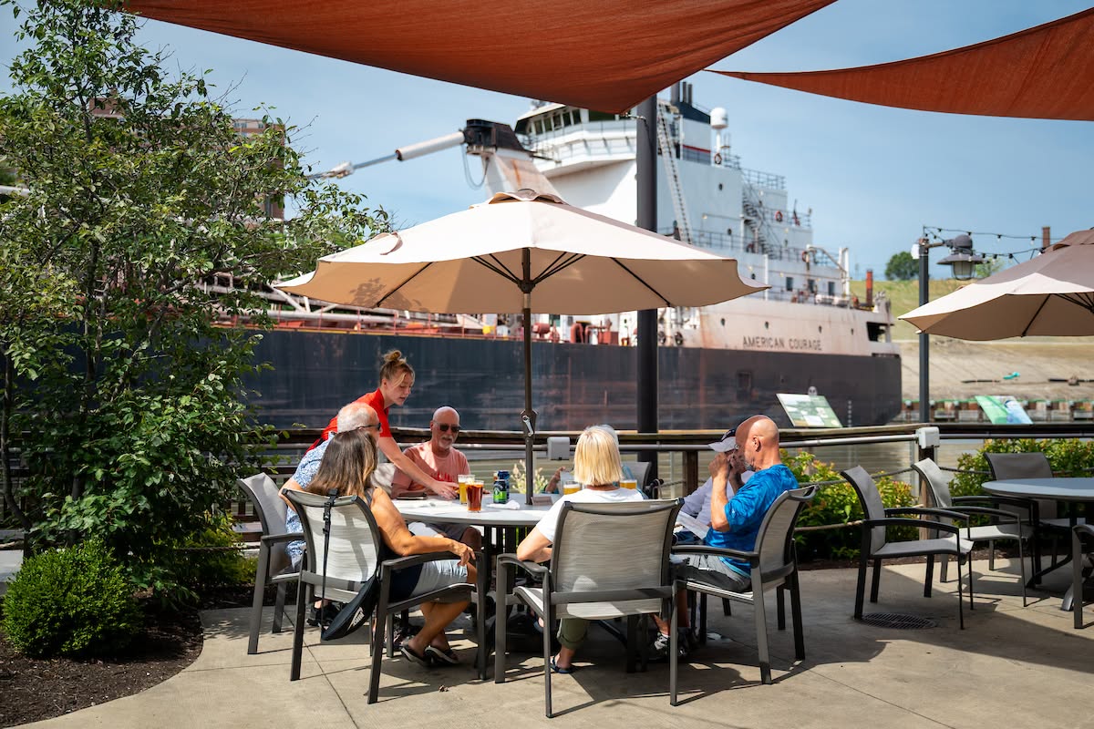 people dining on patio overlooking river with ship