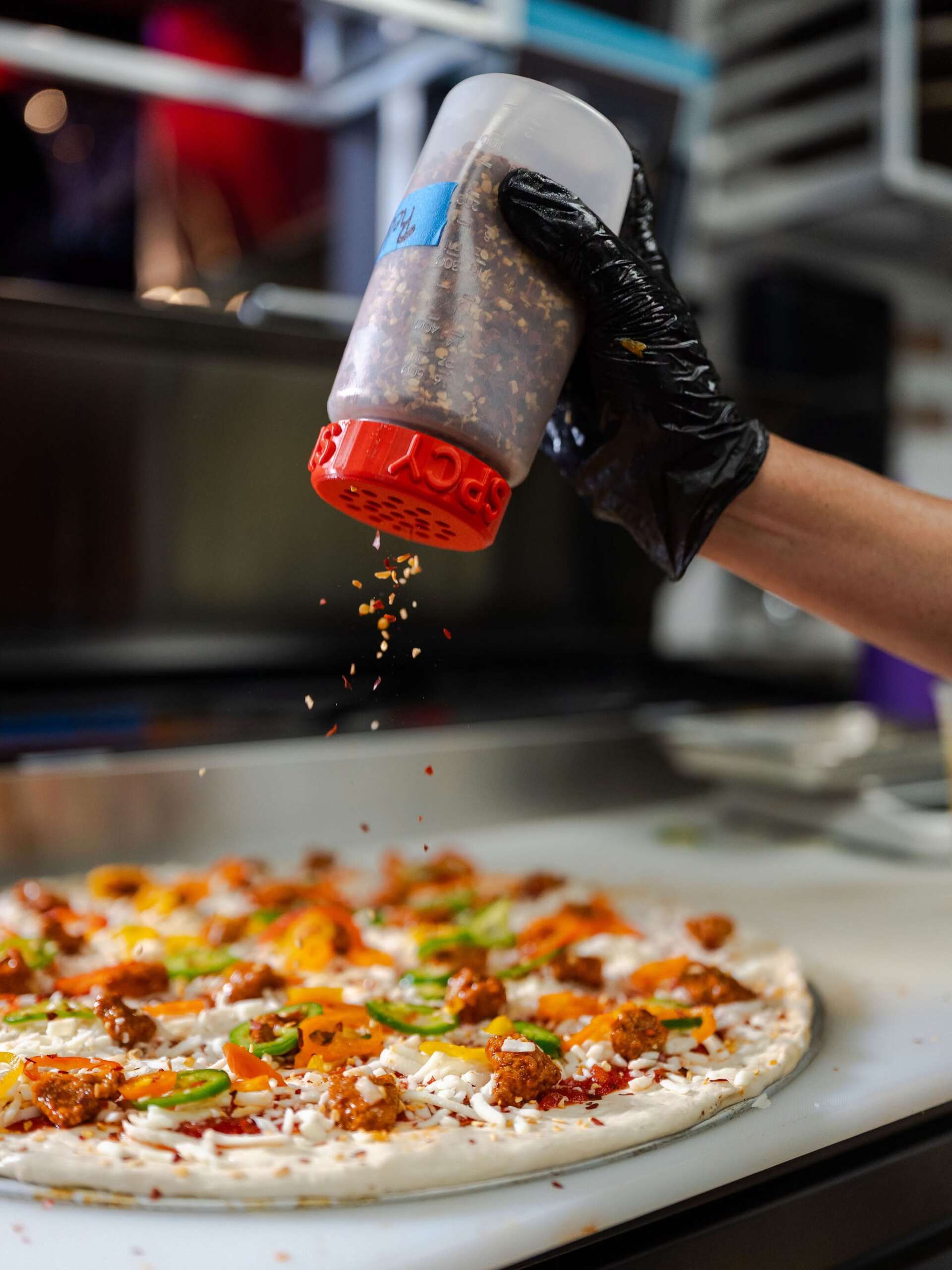 Columbus’ Hottest Pizza Is Back, And There’s A Contest To See Who Can Survive It 1 person shaking crushed peppers on pizza