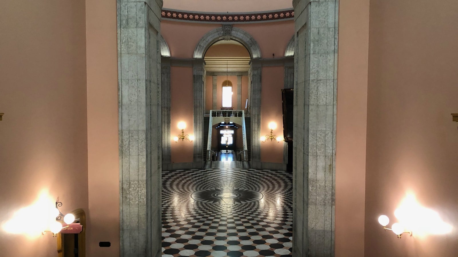 Marble piers frame a view into the Ohio Statehouse rotunda, with its black-and-white patterned floor and glowing brass wall lamps