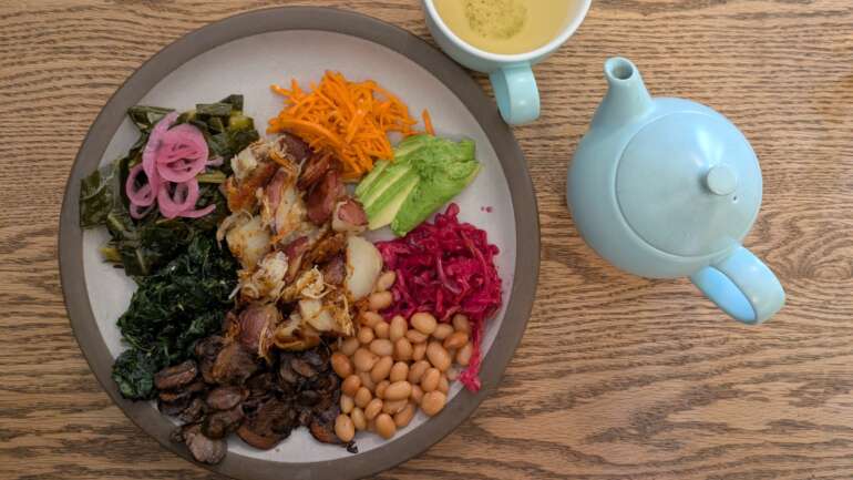 The Best Vegan Restaurants And Plant-Based Menus In Columbus 2 Overhead view of a vegan breakfast plate with roasted potatoes, avocado, white beans, greens and pickled onions beside a pot of tea